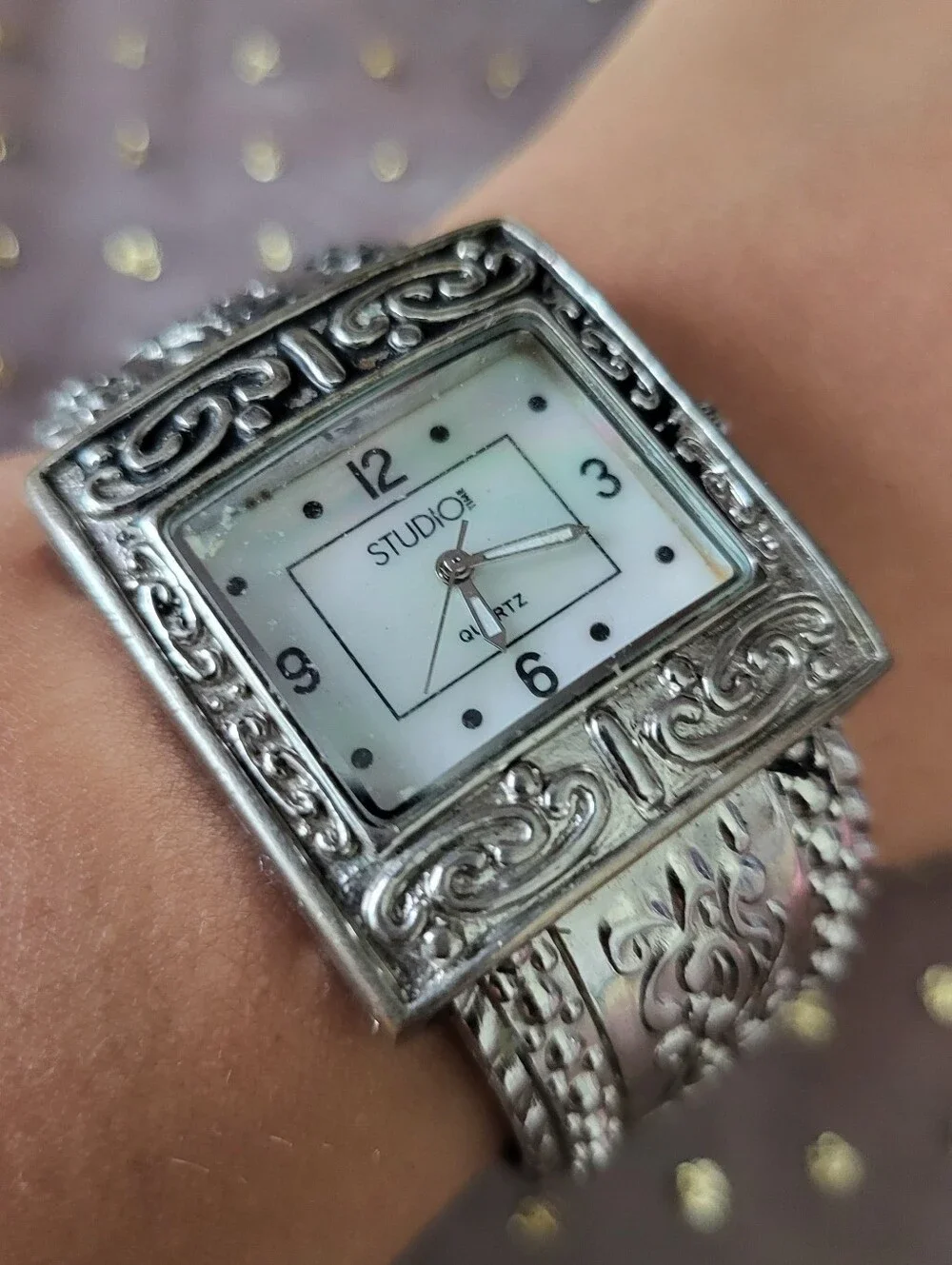 Silver bracelet watch with ornate scrollwork design has antique white face